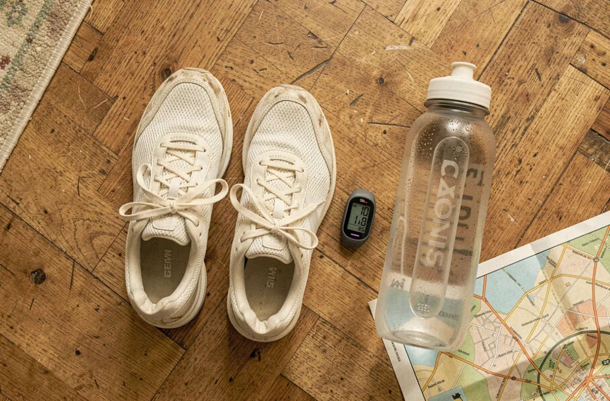 Chaussures de marche, podomètre et gourde posés sur un parquet en bois, préparatifs pour atteindre 10000 pas par jour